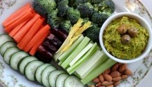 Hummus with broccoli, carrot, dates, celery, almonds, and cucumbers. Green olives garnish the dip.